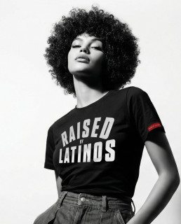 Model wearing the Raised By Latinos black t-shirt off the shoulder, black and white studio shot with red sleeve tab visible