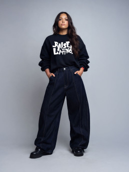 Female model wearing the Champions Crew black sweatshirt with white graffiti logo and wide dark denim, front view