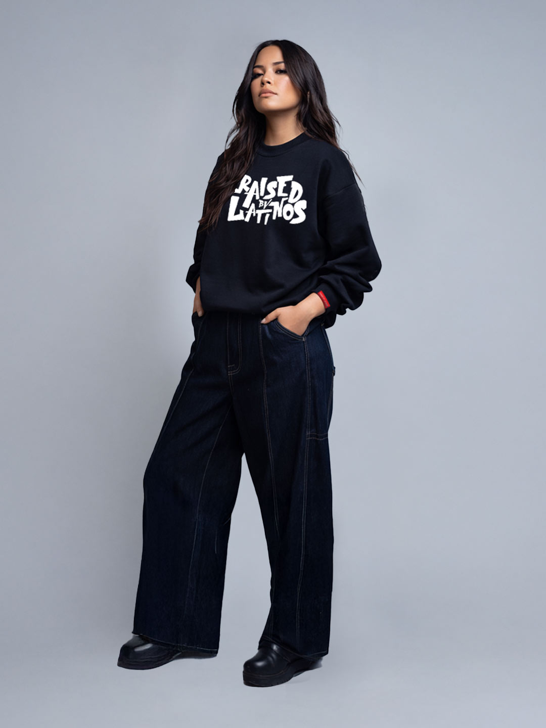 Female model wearing the Champions Crew black sweatshirt, three-quarter view with wide dark denim