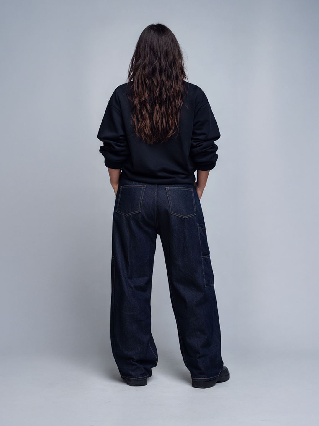 Female model wearing the Champions Crew black sweatshirt, back view with wide dark denim