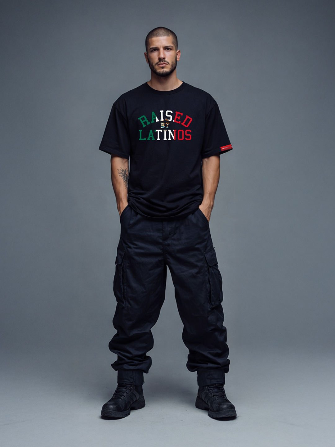 Male model wearing the Firmes y Unidos black t-shirt with green, white and red RAISED BY LATINOS print, front view with cargo trousers