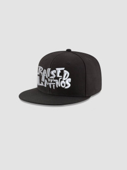 RBL Champions black cap with white graffiti-style RAISED BY LATINOS embroidery, angled view